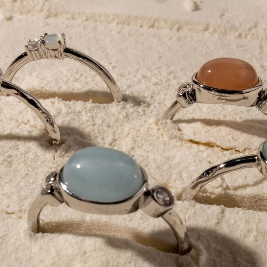 A collection of five sterling silver rings sitting in a sand base