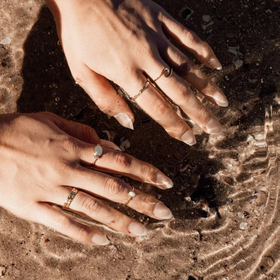 Two hands dipping into water at the beach with a range of different rings on fingers
