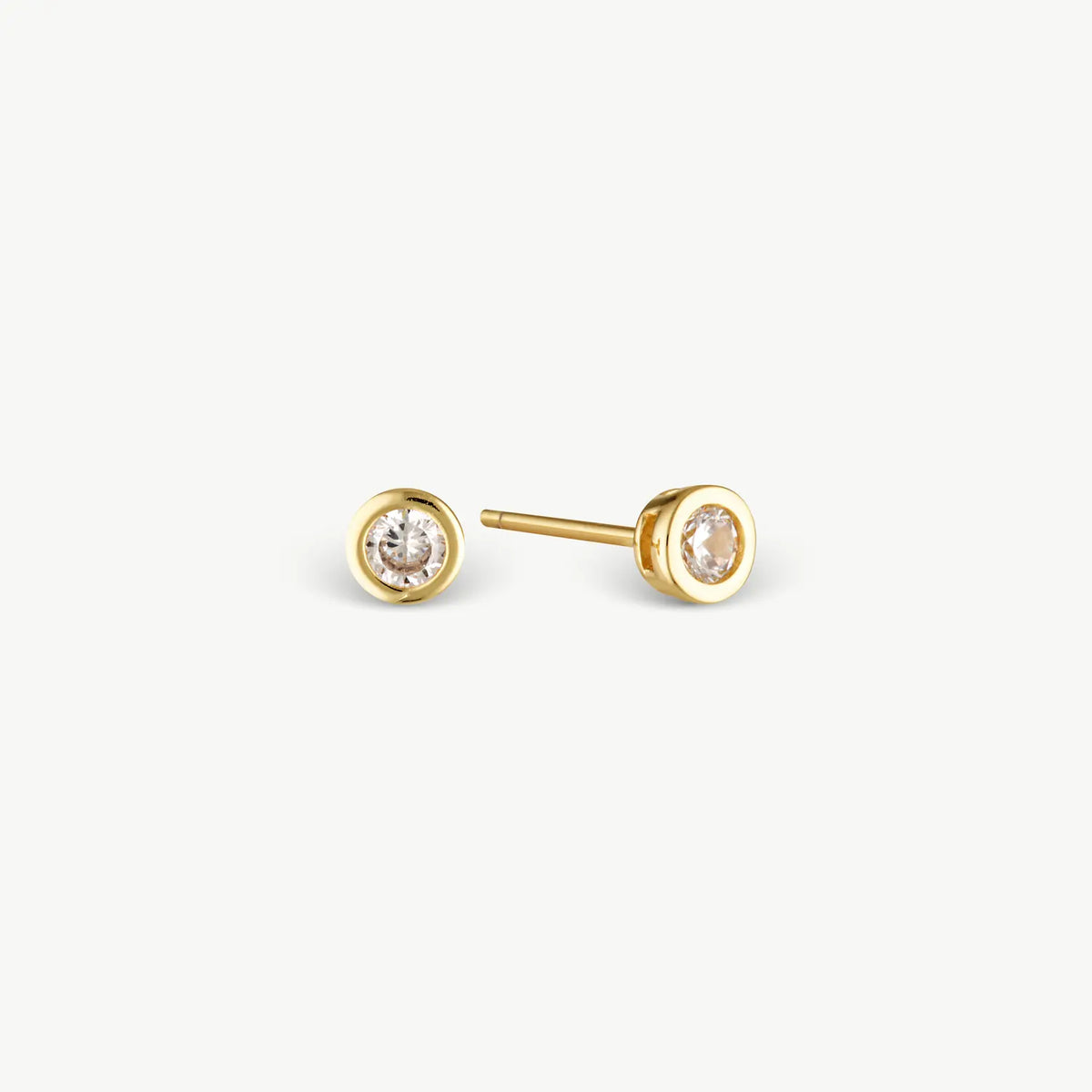 A pair of gold stud earrings with round bezel settings holding clear round-cut gemstones, shown on a clean off-white background.