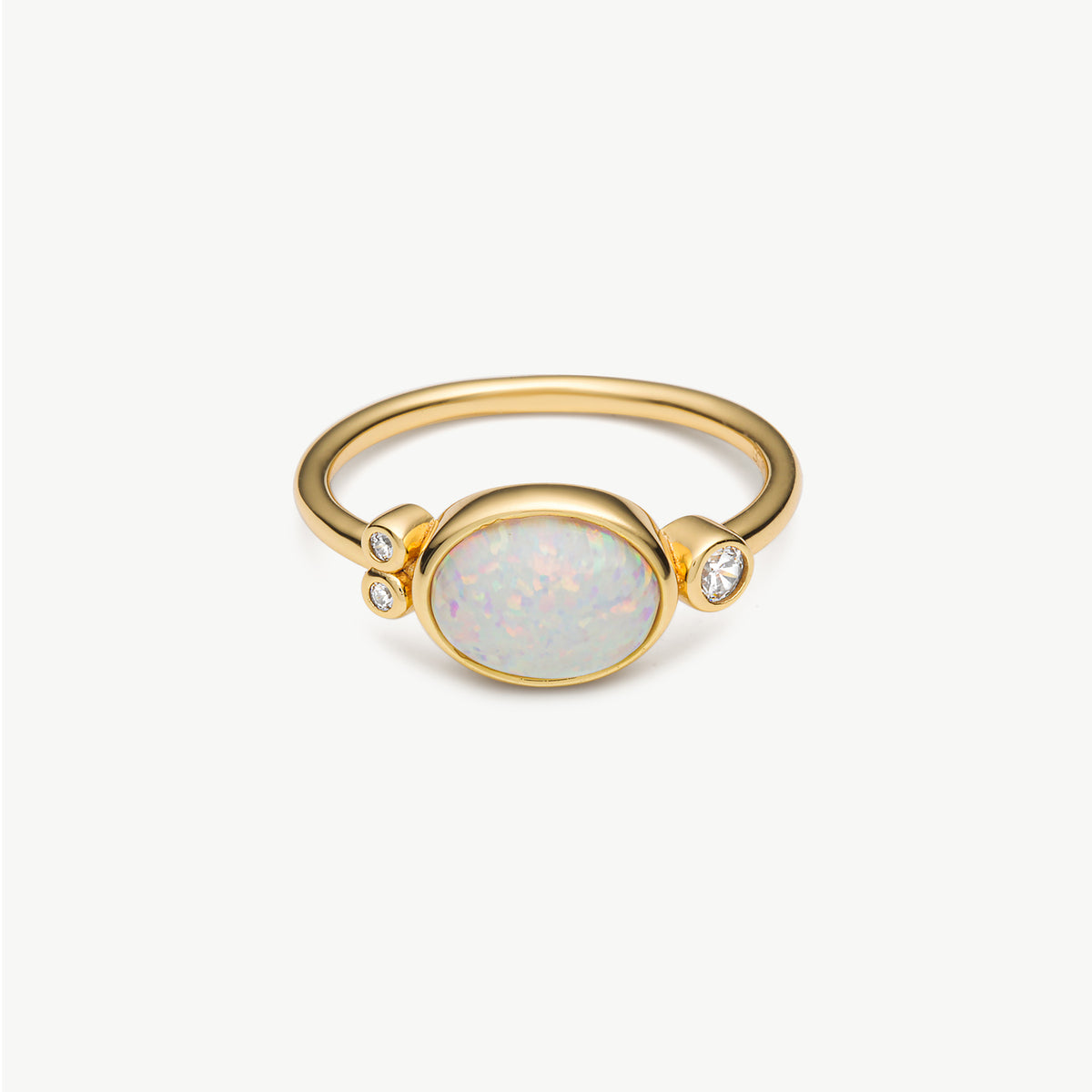 A gold ring featuring an oval white opal center stone and two small clear accent stones, shown on a clean white background.