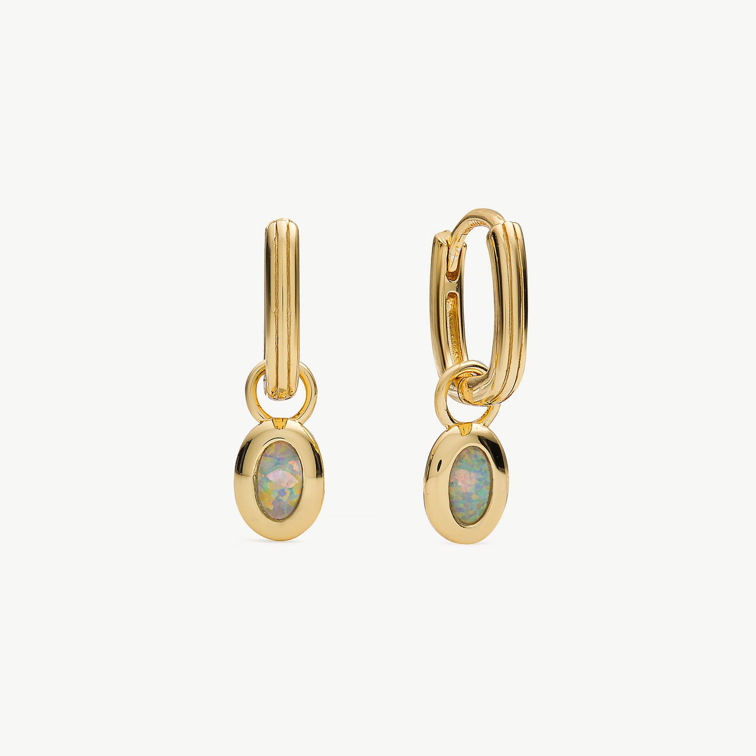 A pair of gold huggie hoop earrings with oval opal gemstone charms, displayed on a clean off-white background.