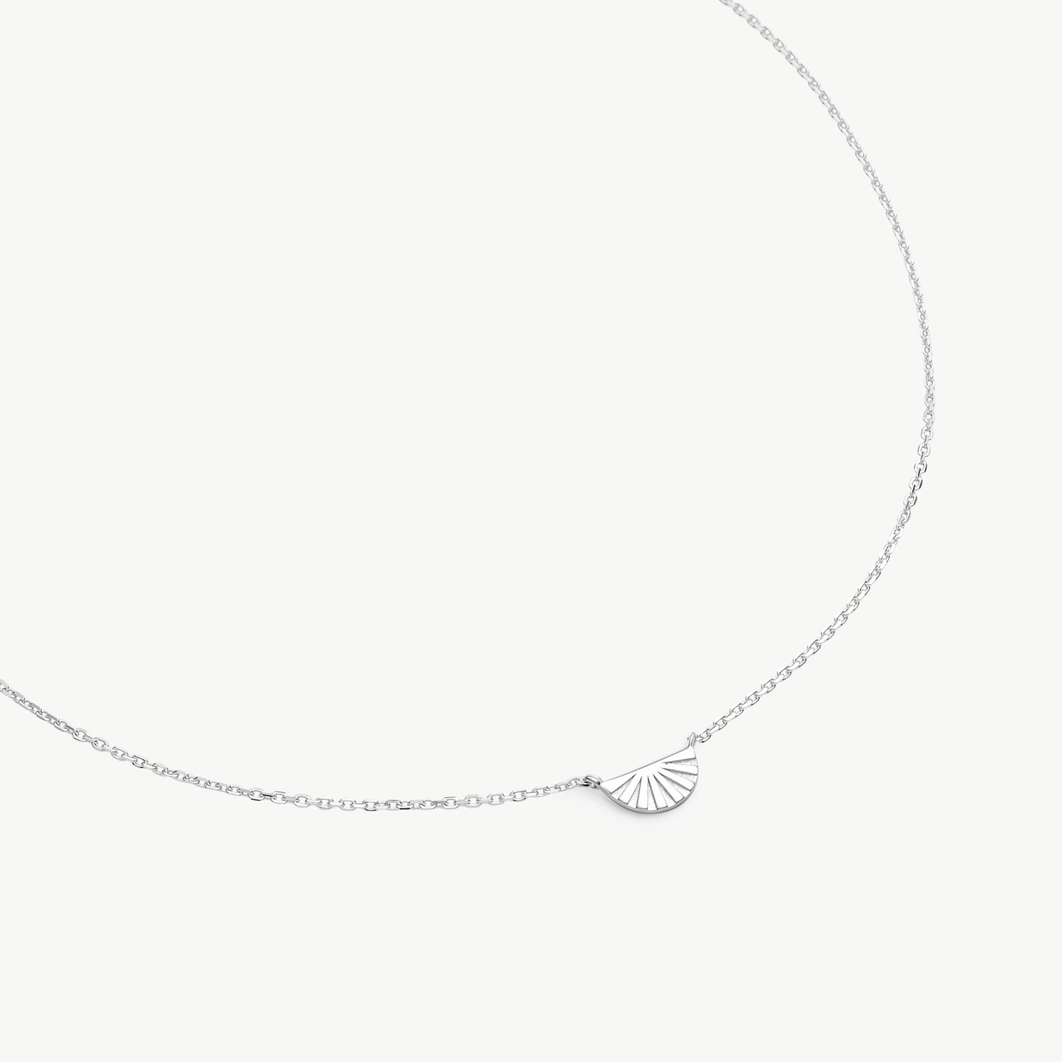 A delicate silver chain necklace featuring a small, fan-shaped shell pendant, displayed against a clean, light off-white background.