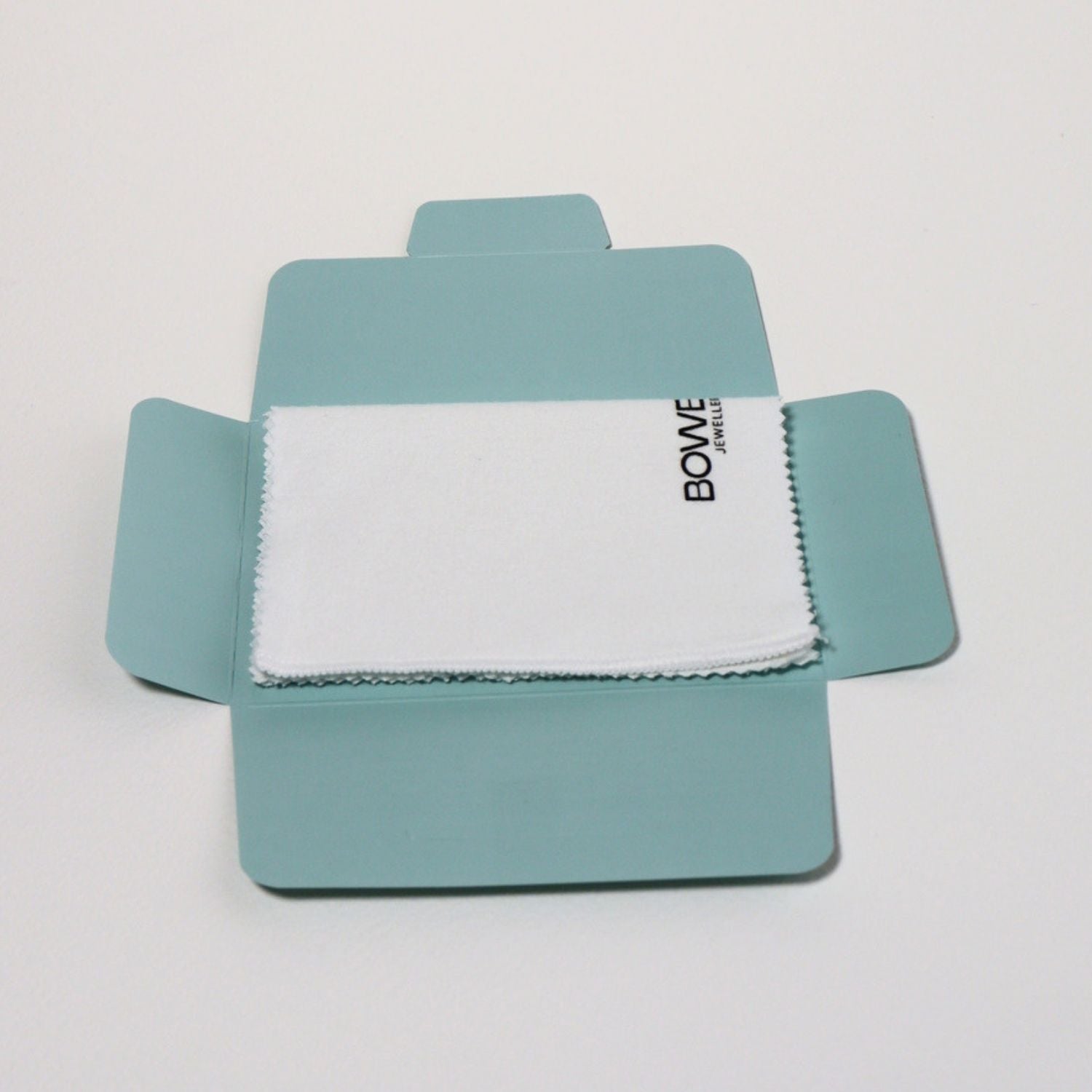 A white microfiber cloth with black 'BOWE' branding, neatly folded inside an open light blue cardboard presentation box on a clean white background.