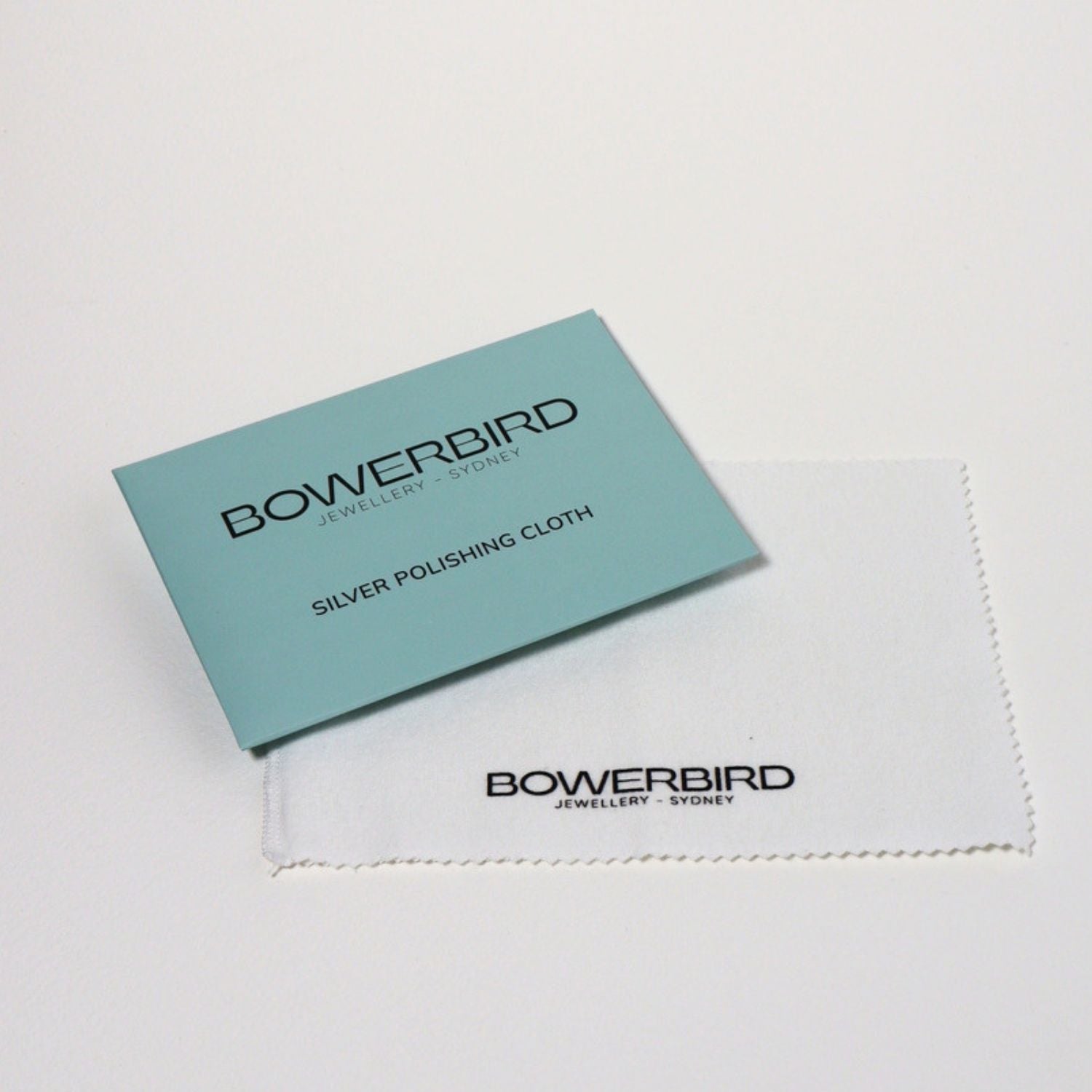 A Bowerbird Jewelry & Stone silver polishing cloth set, featuring a light blue card and a white microfiber cloth on a clean white background.