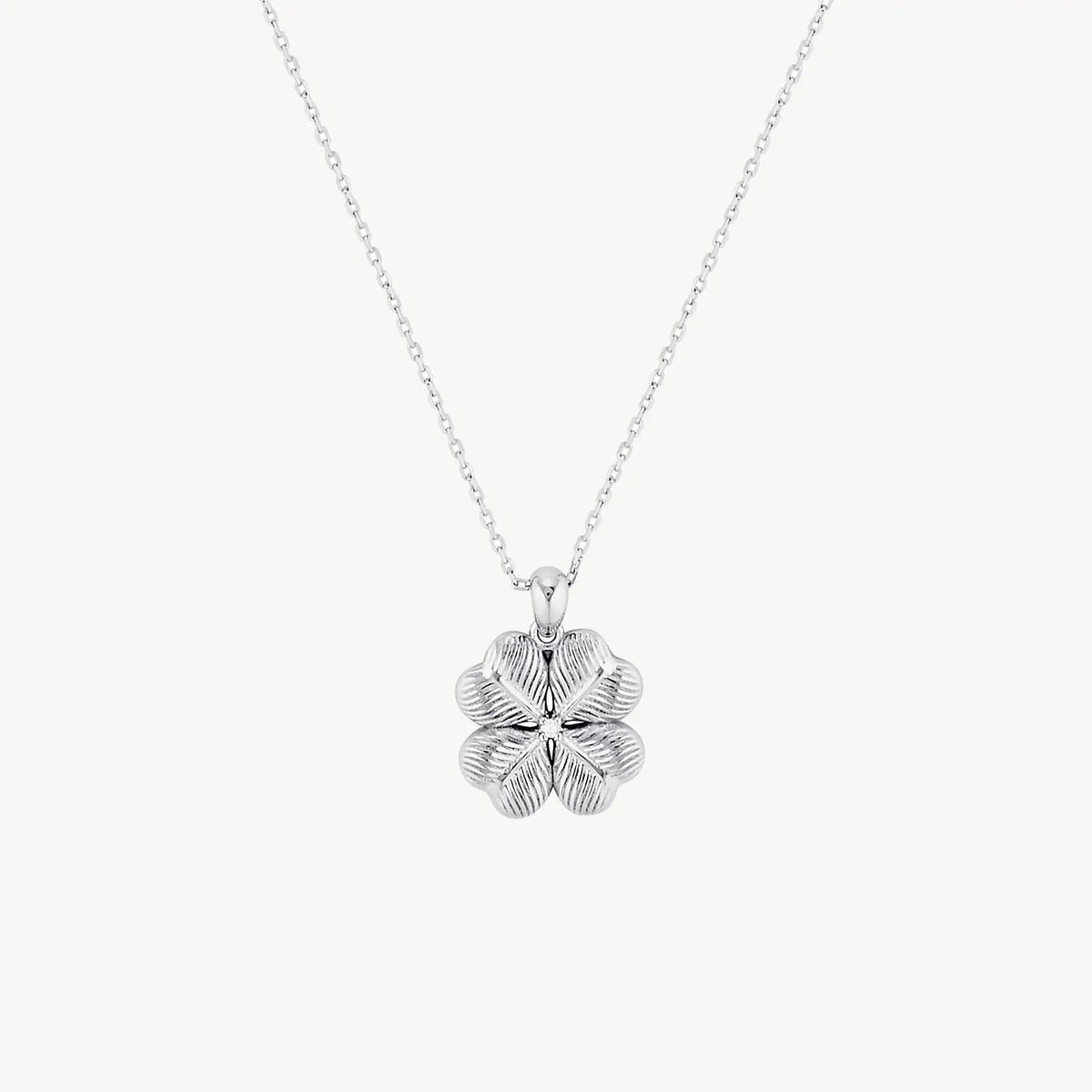 A ridged four-leaf clover with a white stone centre hanging from a silver-coloured chain on a cream background