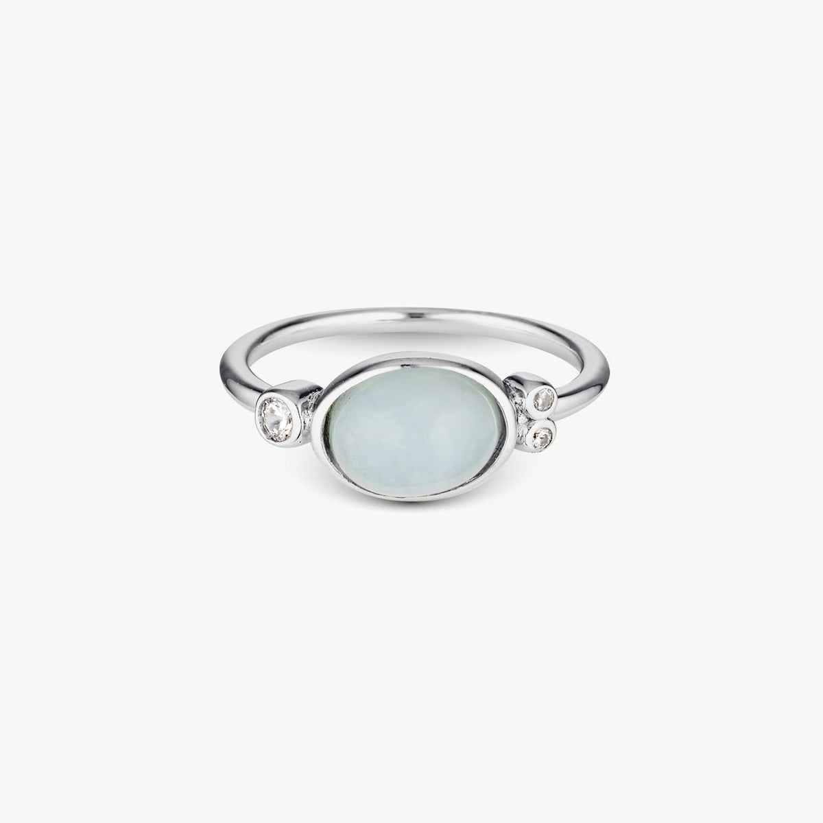 A silver ring featuring a large oval pale blue stone in the center, flanked by two small clear stones on each side, set against a plain light background.