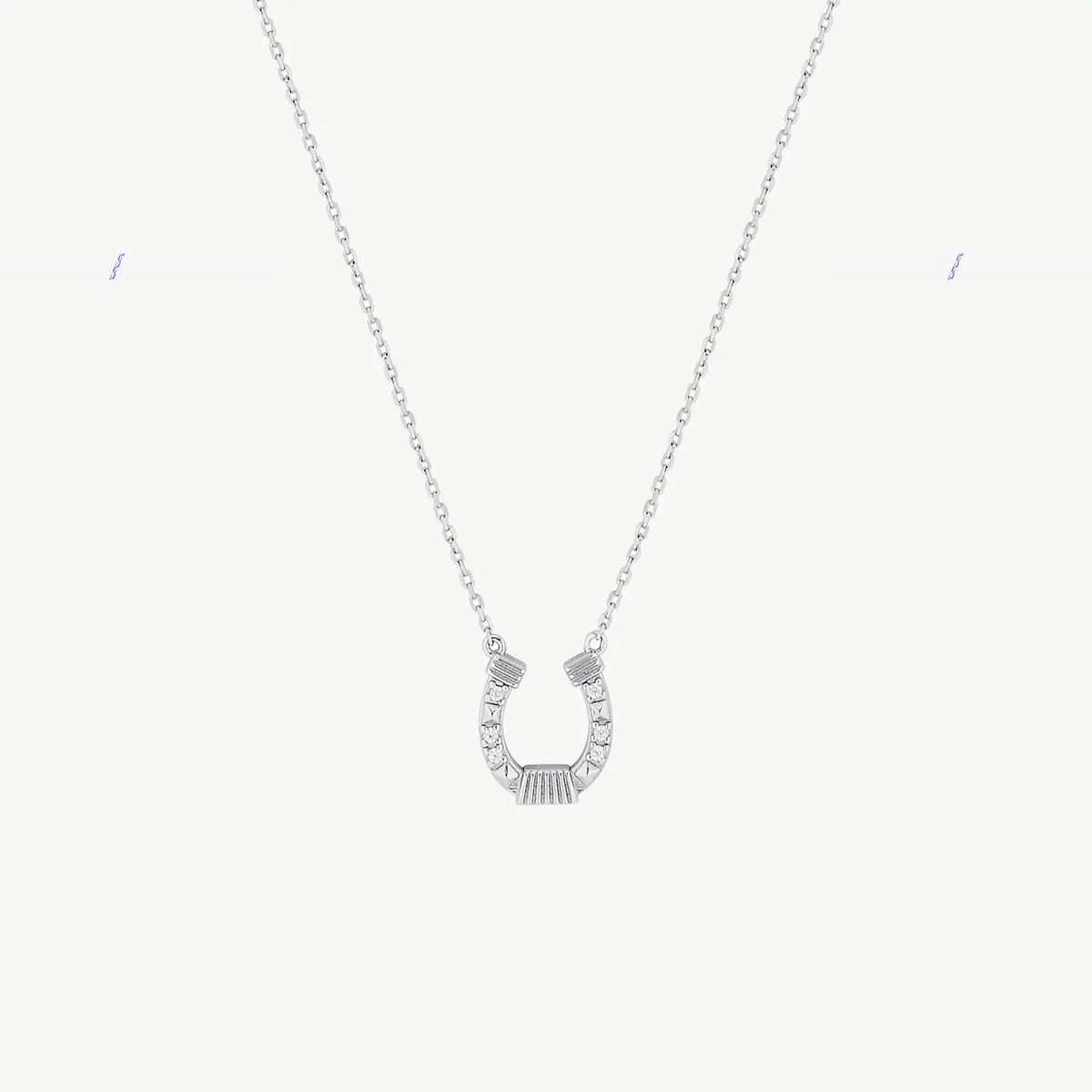 A hanging silver horseshoe charm suspended from a fine cable chain with cubic zirconias on a cream background
