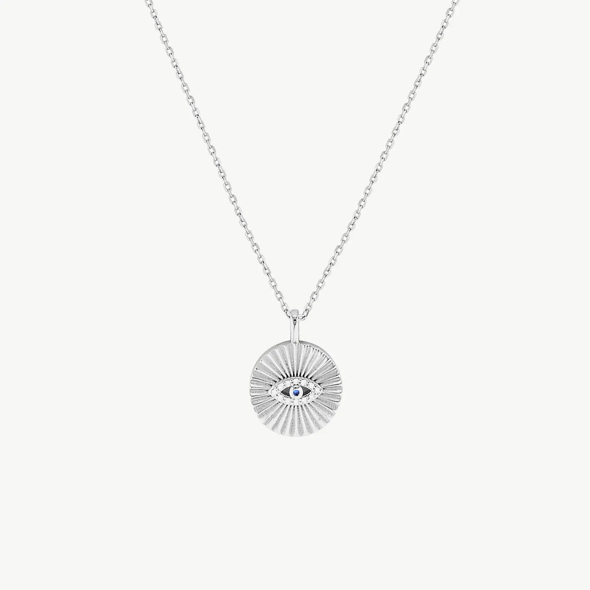 A sparkling Evil Eye motif on a radiating disc background in silver, suspended from a silver chain on a cream background