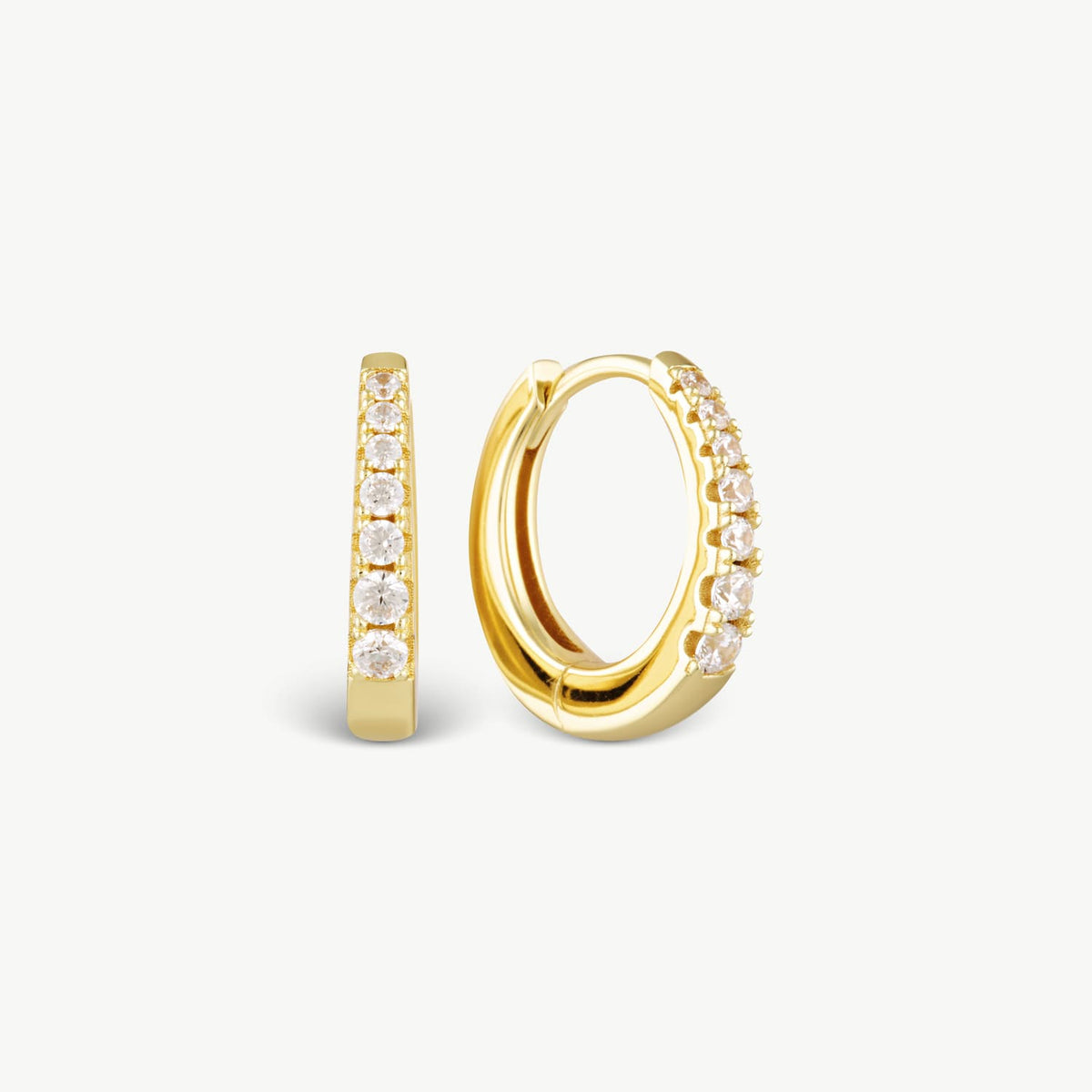 A pair of gold huggie hoop earrings with clear round-cut stones set along the front, shown on a clean off-white background.