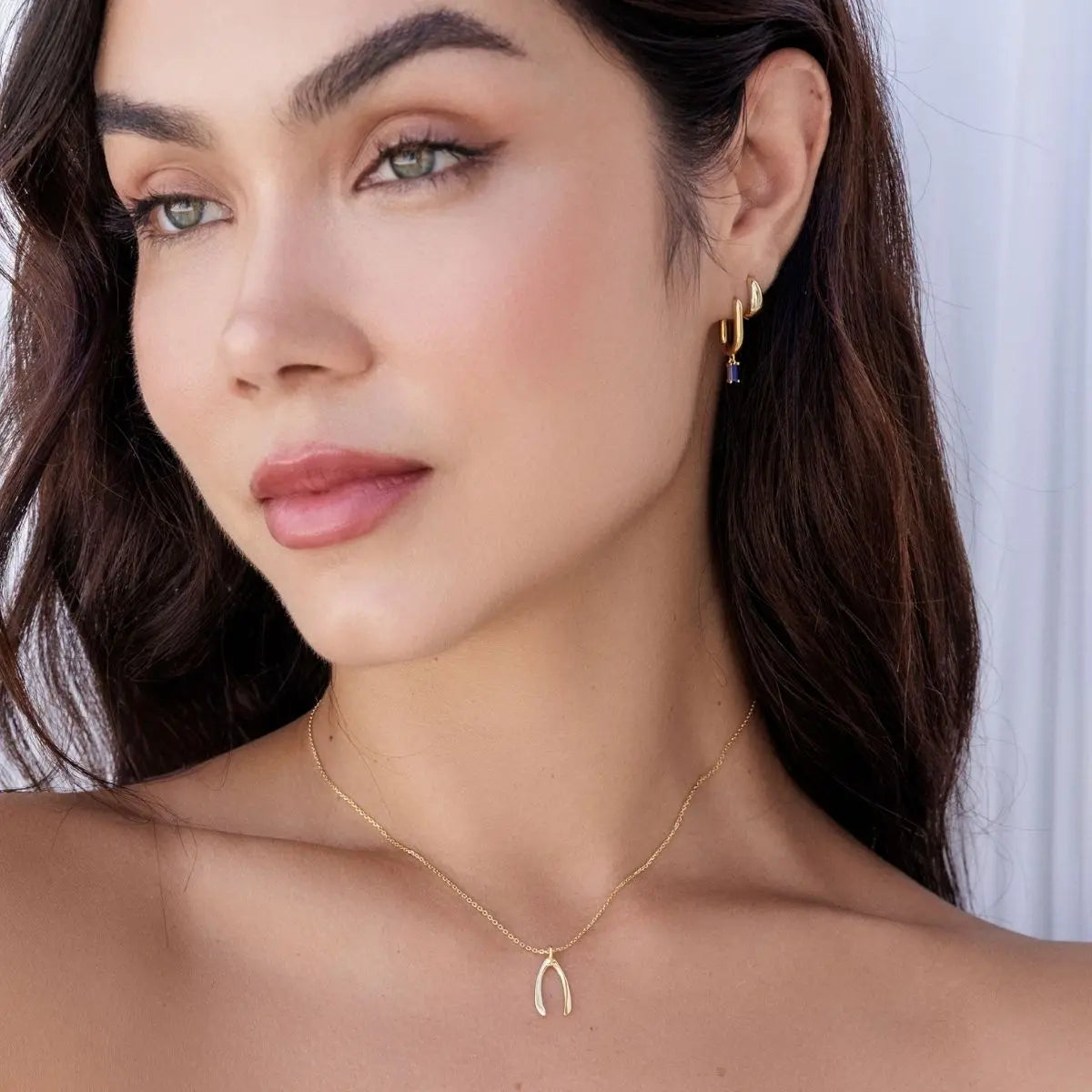 Close-up of a woman wearing gold earrings and a necklace with a wishbone pendant.