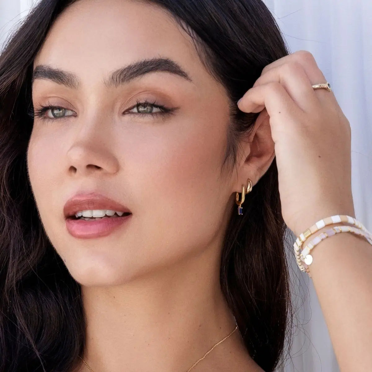 Woman wearing gold earrings and bracelets with a neutral background