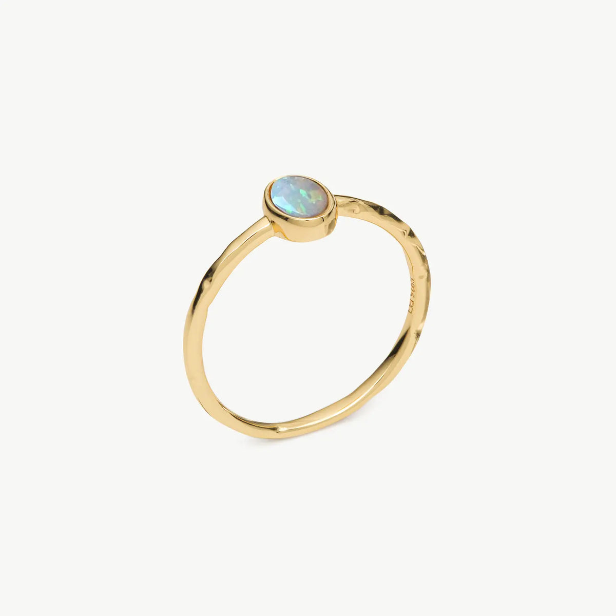 A gold ring featuring a small, bezel-set oval opal stone with iridescent blue, green, and white play-of-color, shown on a clean off-white background.