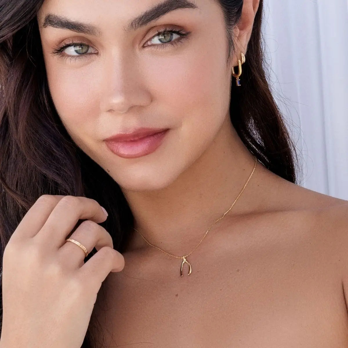 Woman wearing a gold necklace with a small pendant, close-up of her neck and hand.