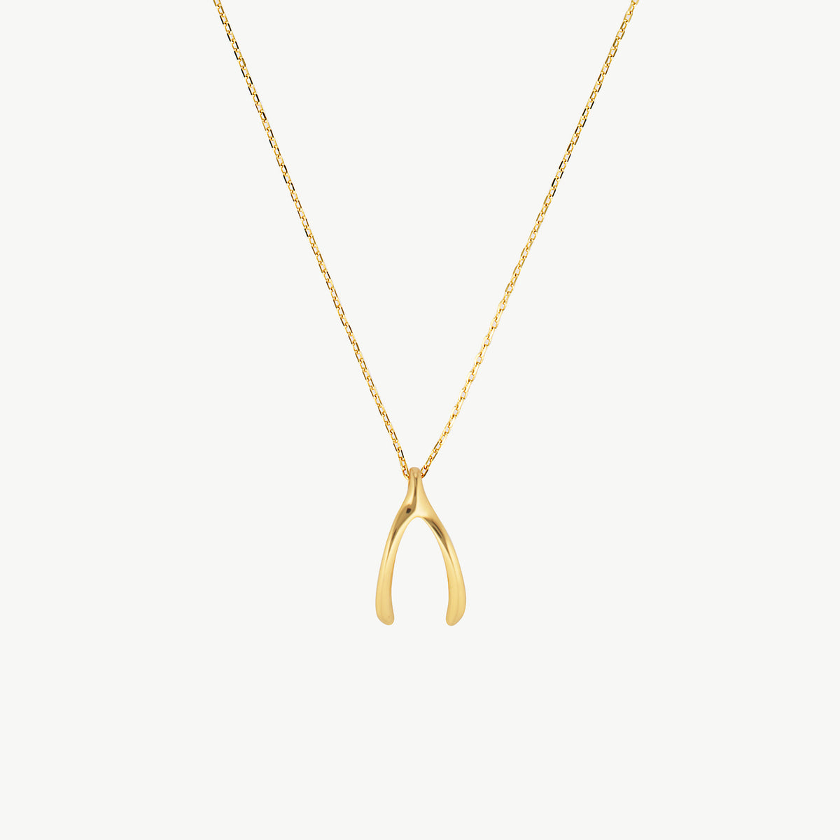 A delicate gold chain necklace featuring a small, polished gold wishbone pendant, displayed against a clean, off-white background.