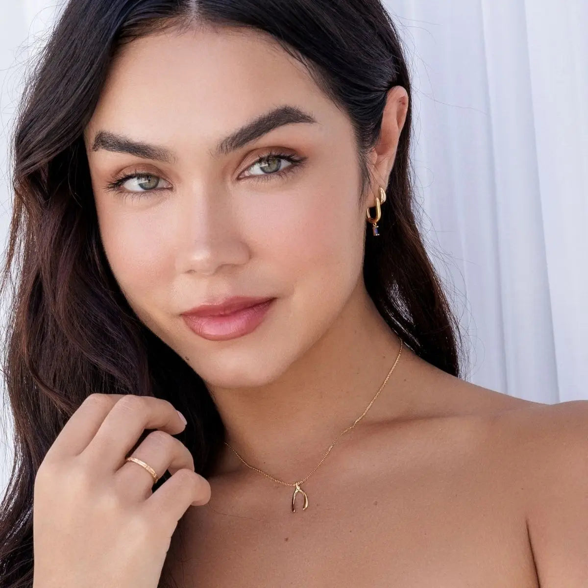 Woman wearing a gold necklace and earrings against a white background
