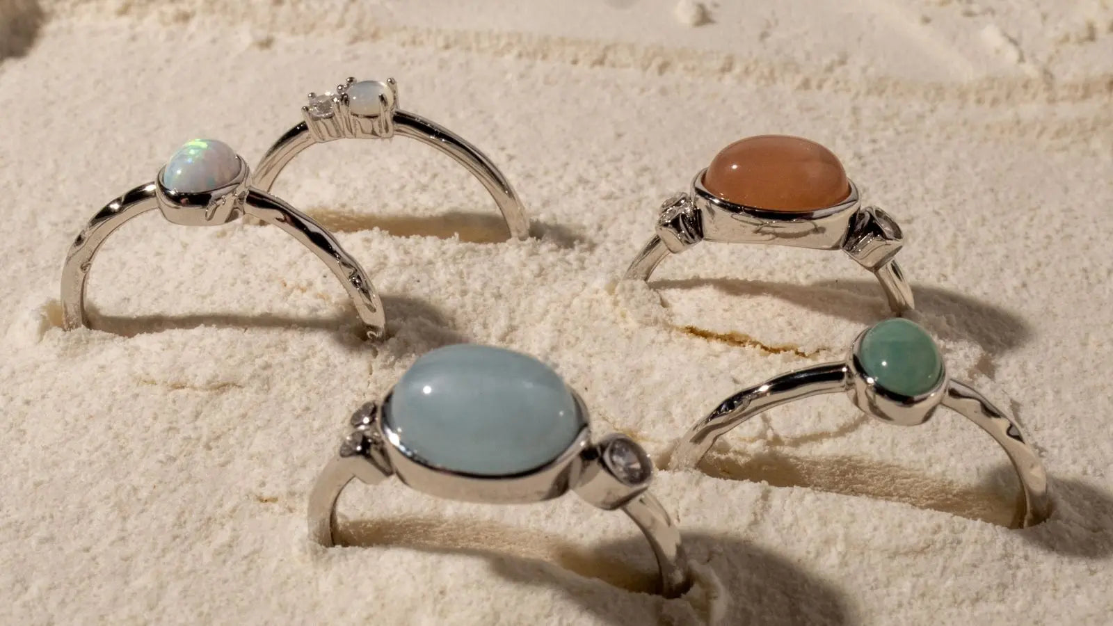 A collection of five sterling silver rings sitting in a sand base 
