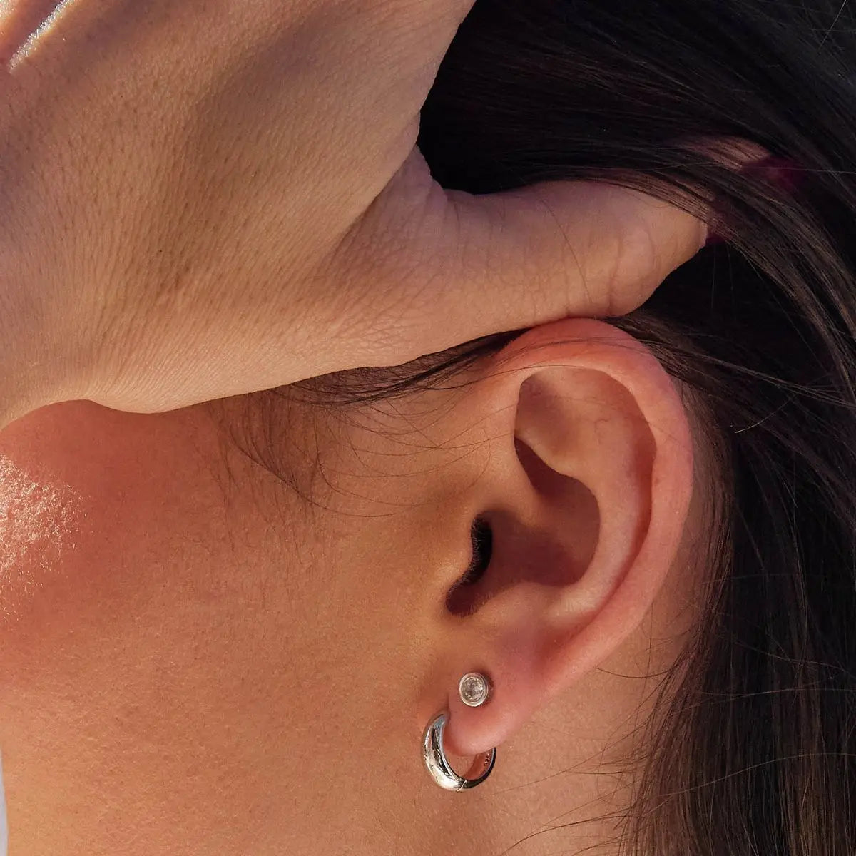 Close-up of a person wearing a silver hoop earring with a blurred background