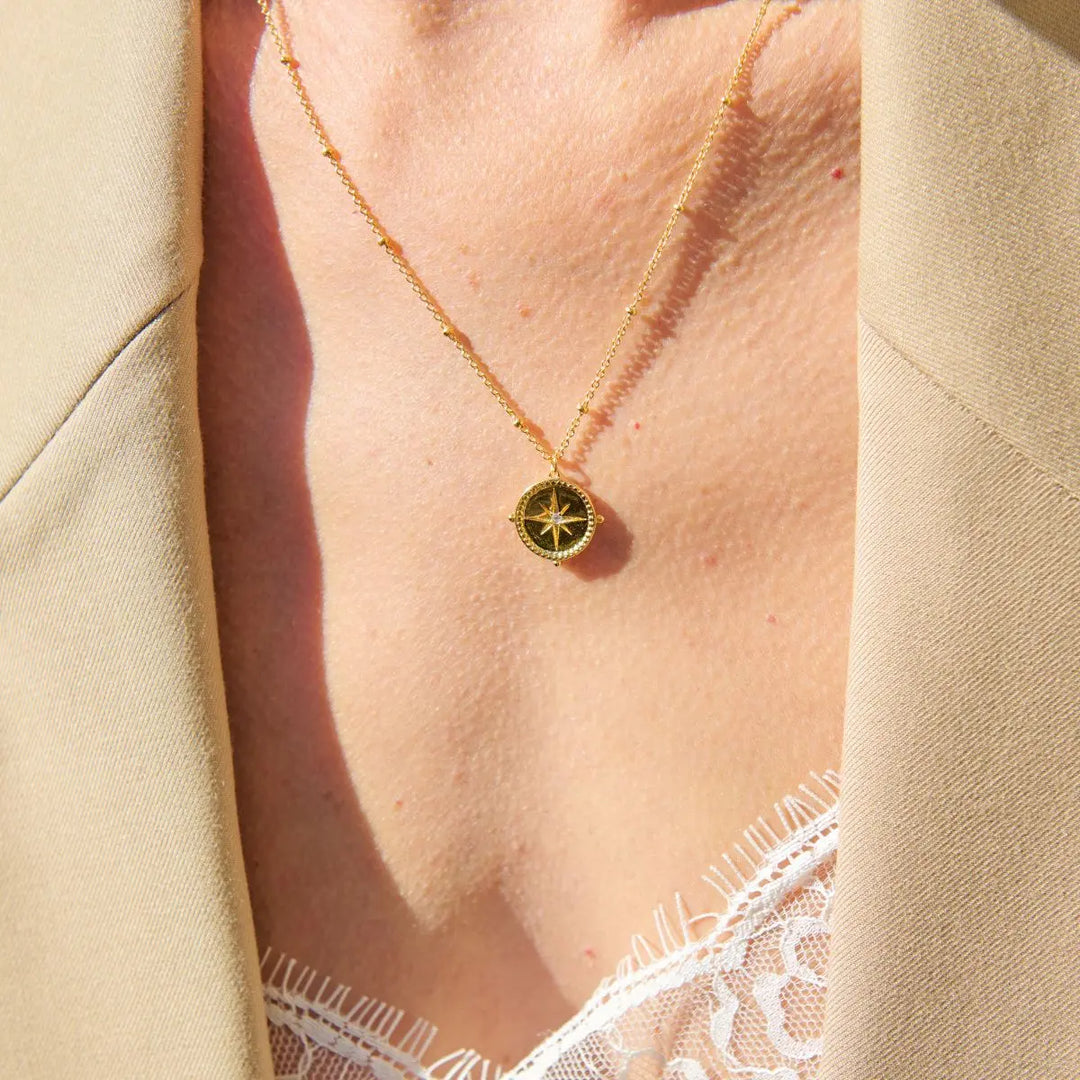 Necklace with a compass pendant worn by a person, with a beige background