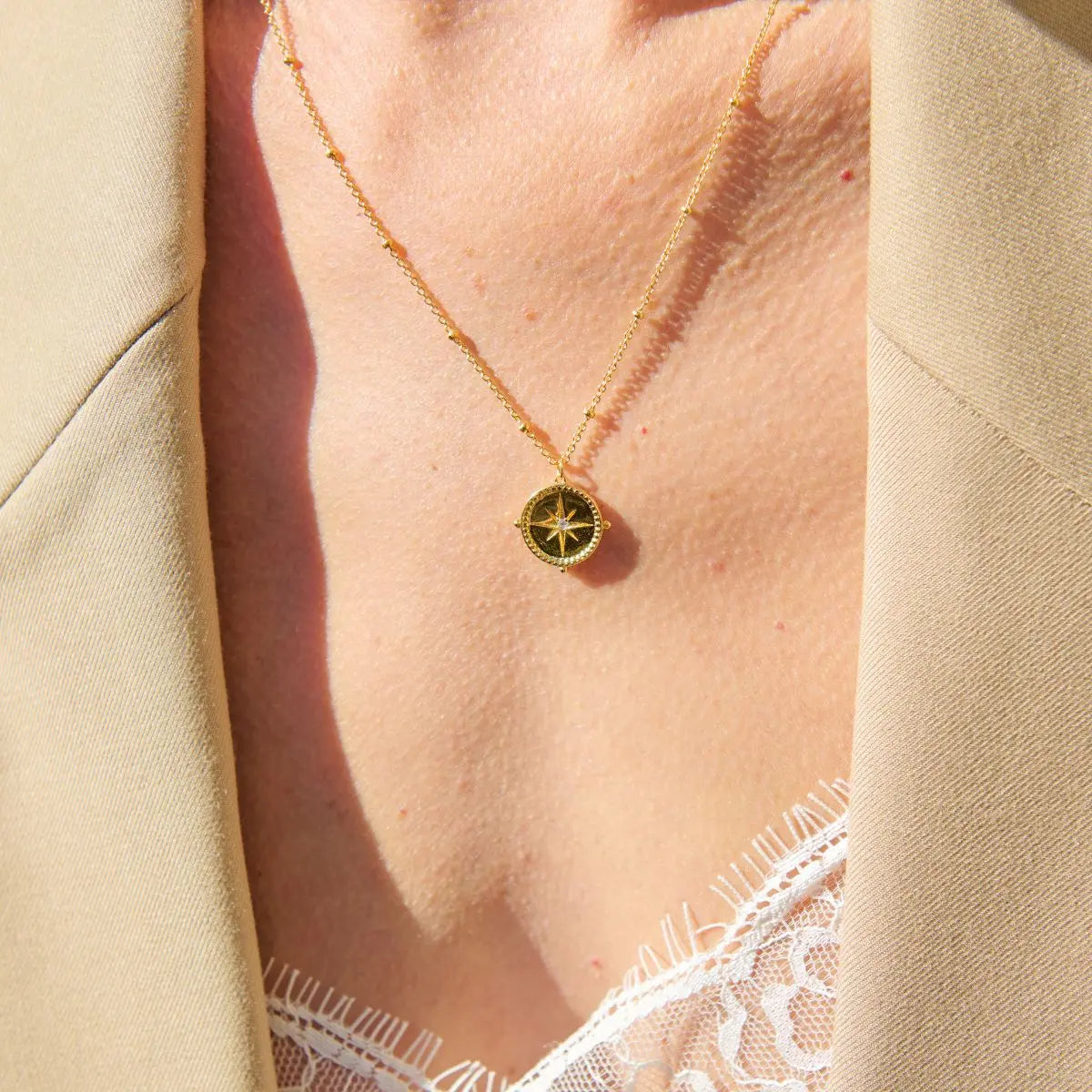 Necklace with a compass pendant worn by a person, with a beige background