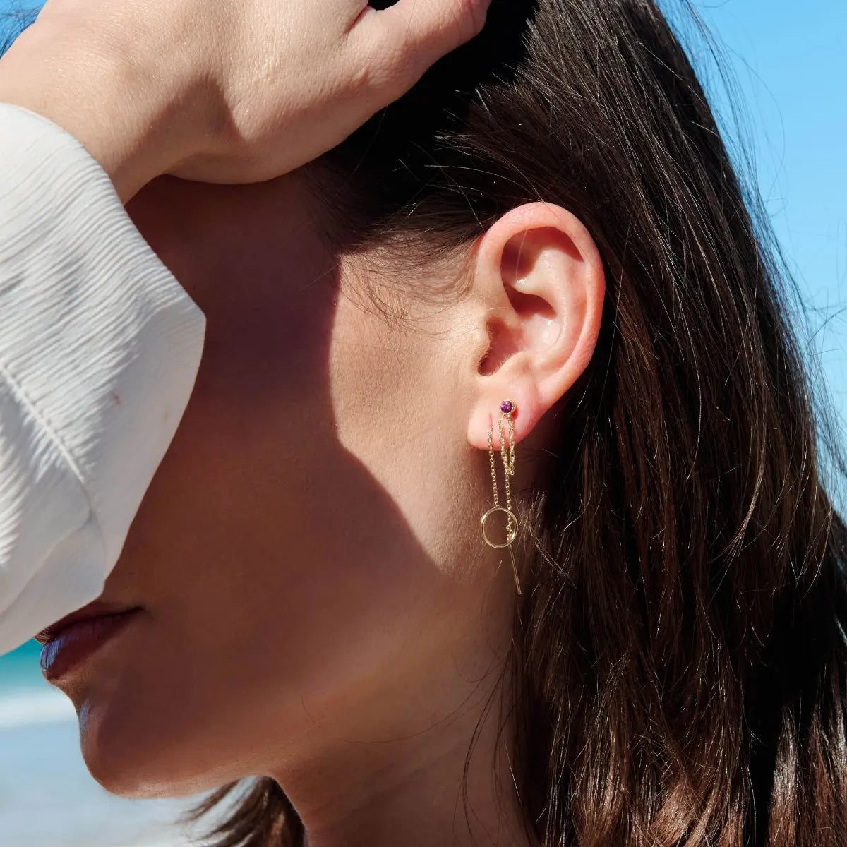 Close-up of a person wearing gold hoop earrings with a blue sky background