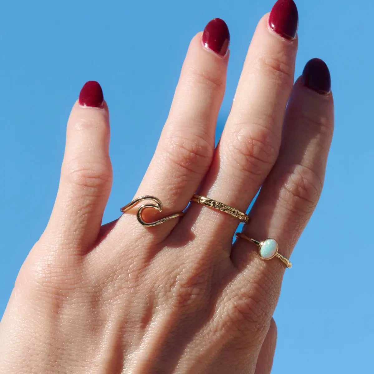 Hand wearing three gold rings with a clear blue sky background