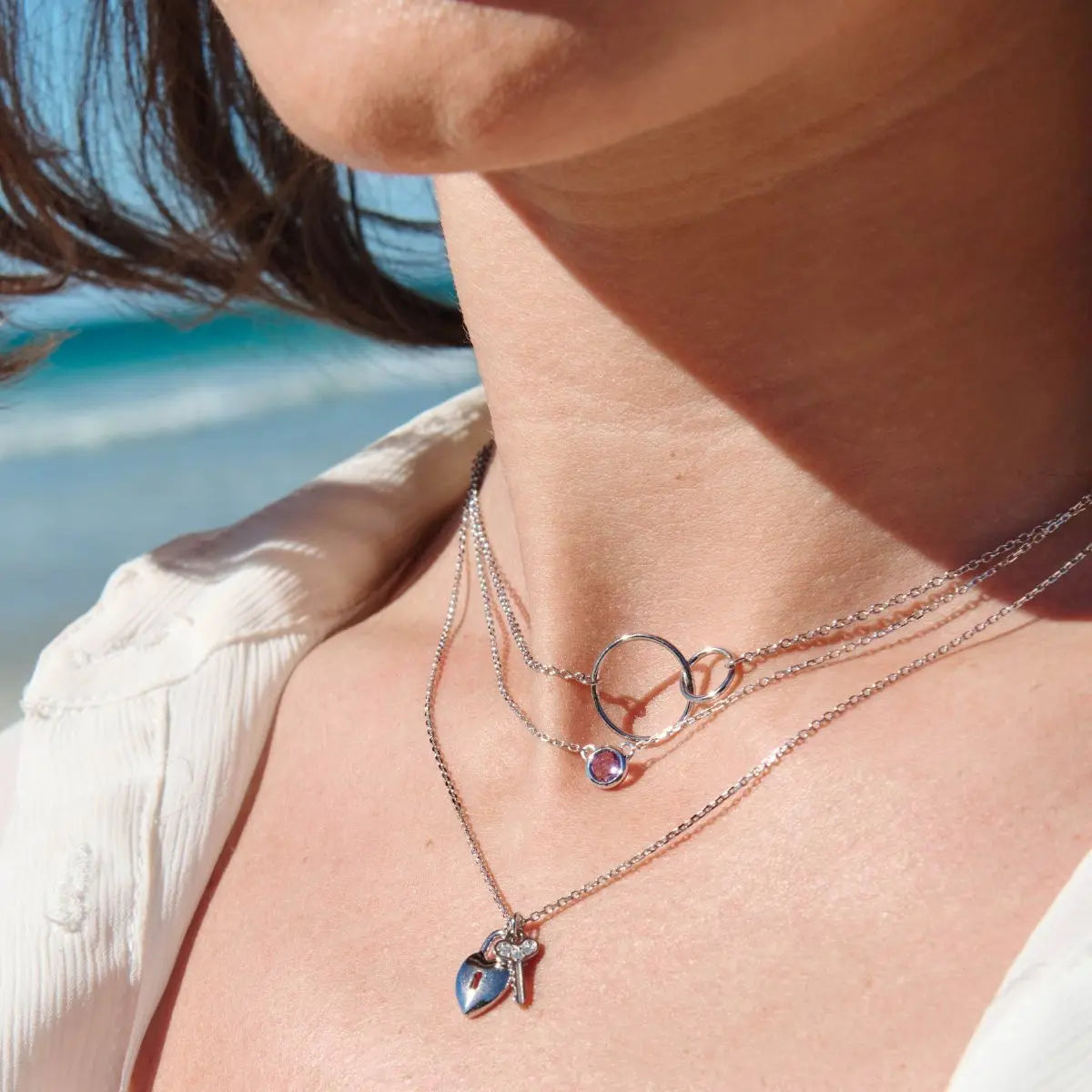 Close-up of a person wearing multiple necklaces with a beach in the background