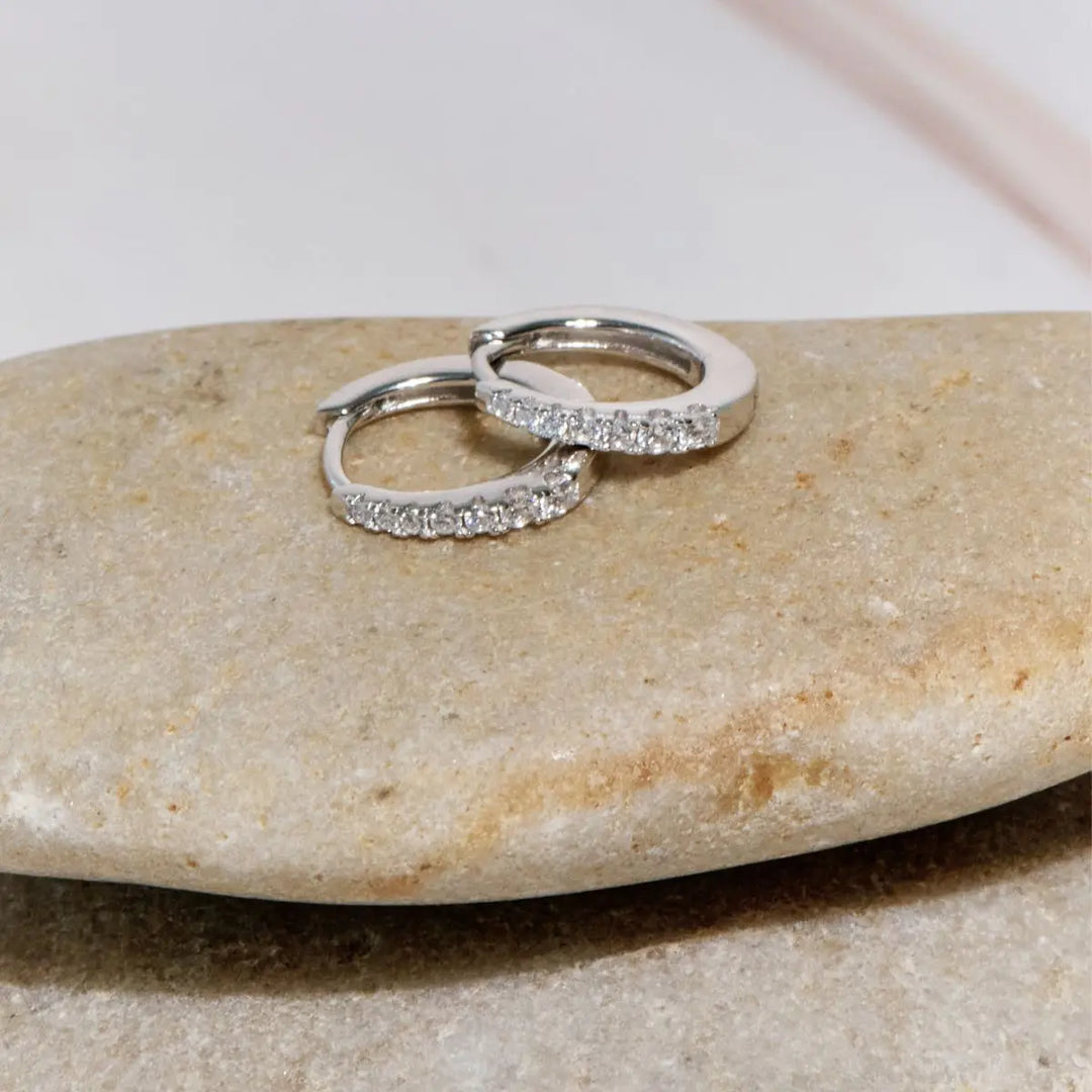 Two silver earrings with small diamonds on a beige stone.