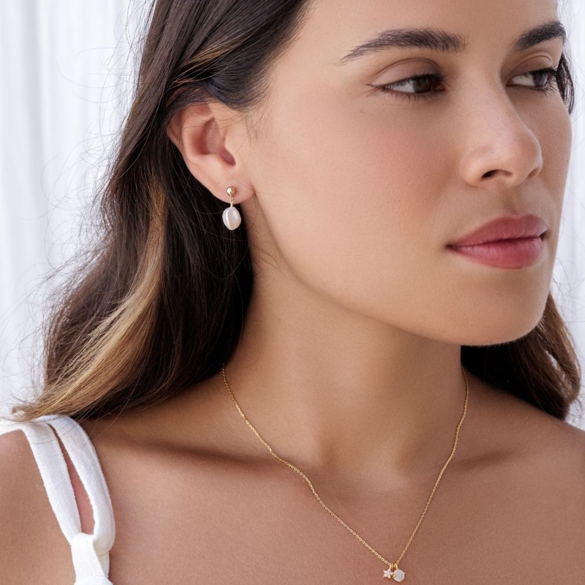 Close-up of a woman wearing pearl earrings and a gold necklace against a white background