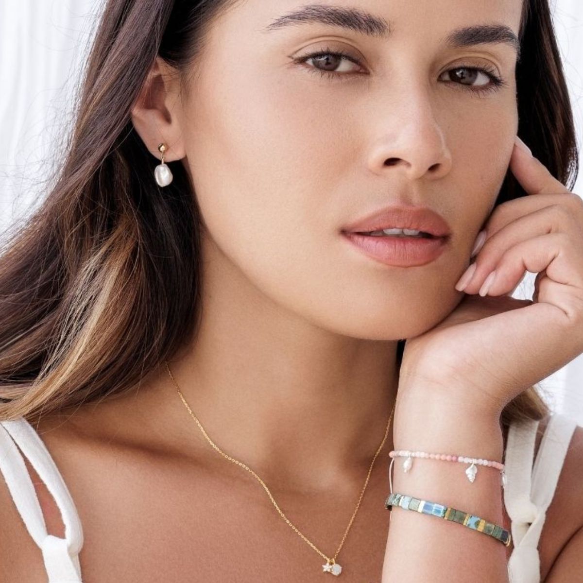 Woman wearing a gold necklace, pearl earring, and colorful bracelets on a white background