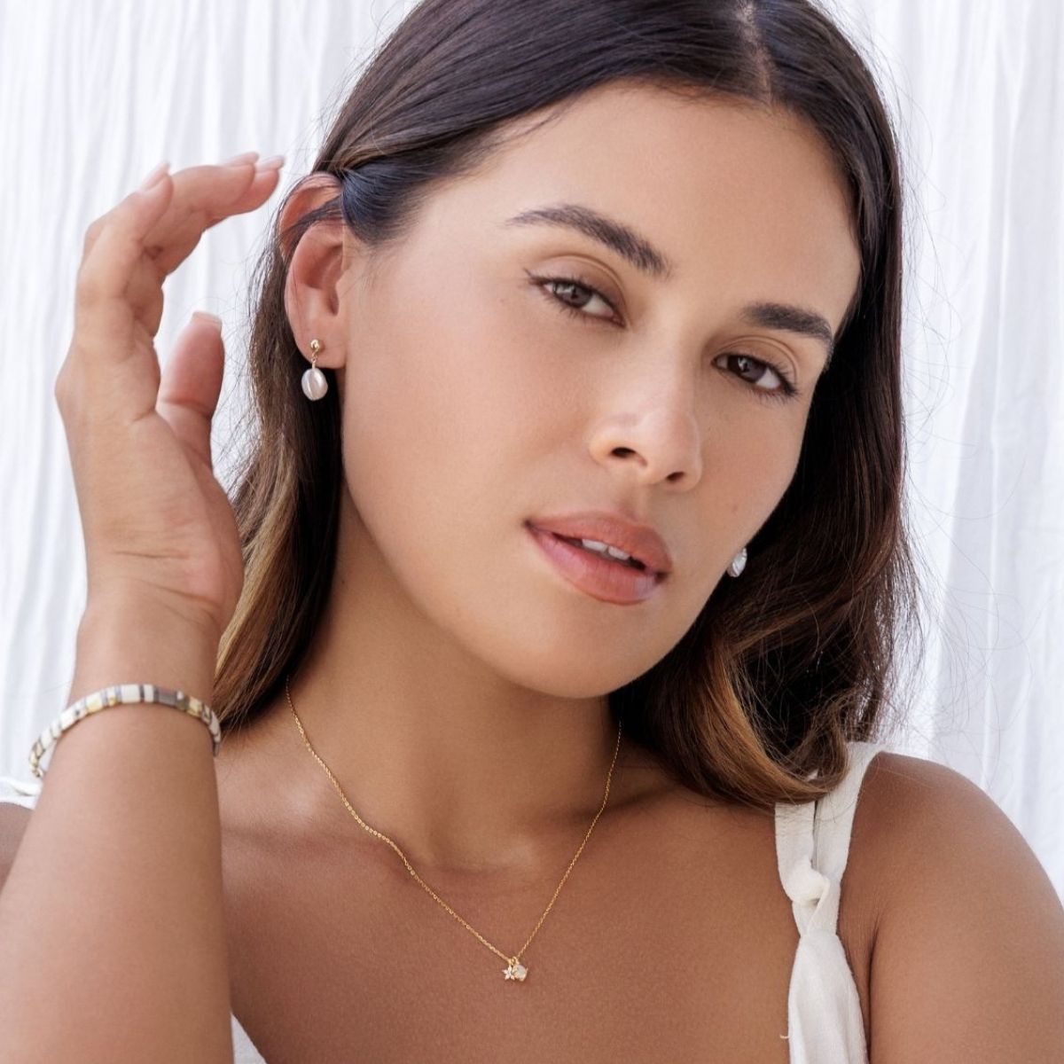 Woman wearing a gold necklace and earrings with a white background