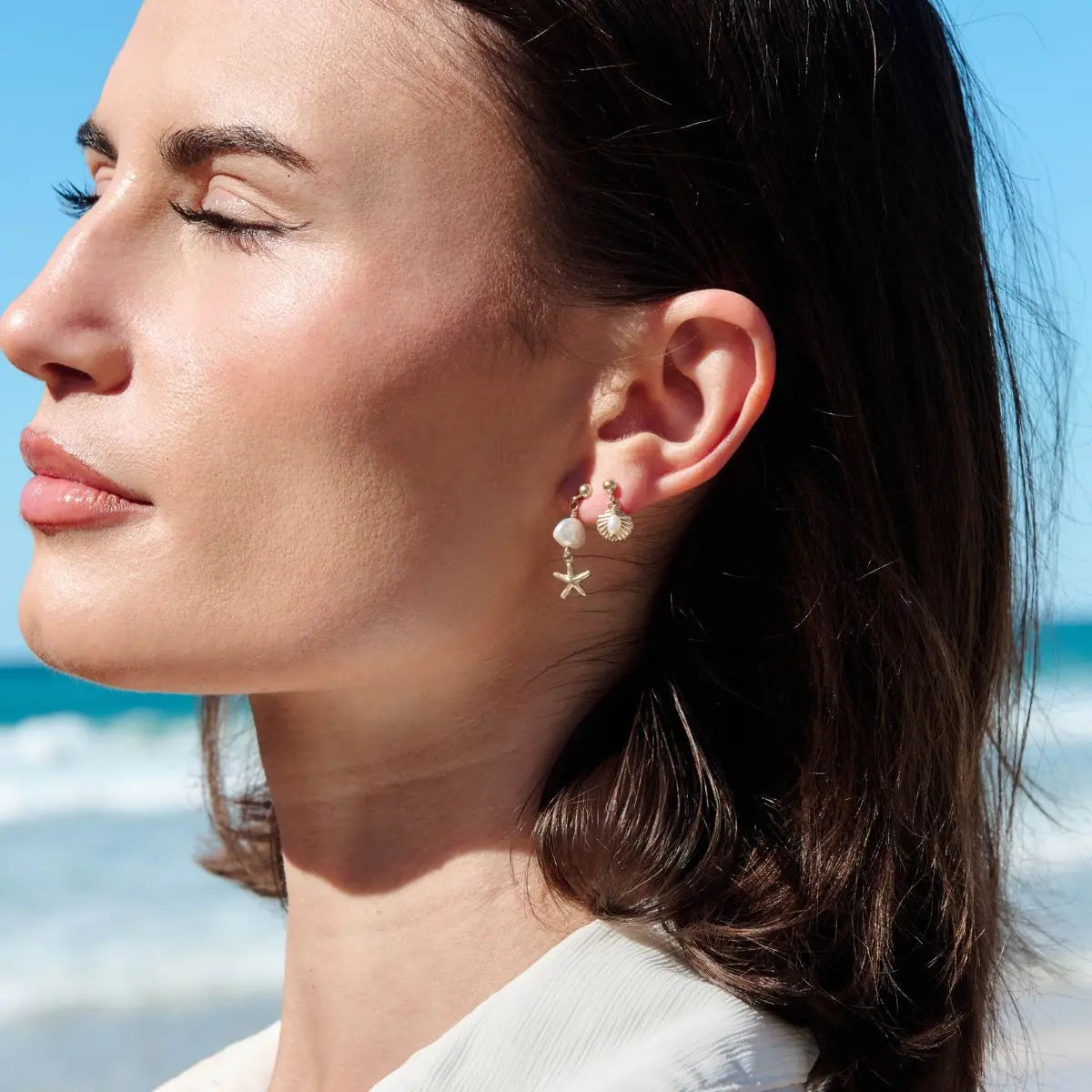Close-up of a woman wearing pearl and starfish earrings with a blurred beach background