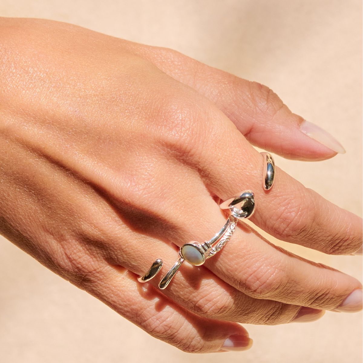 Hand wearing multiple silver rings with a soft beige background