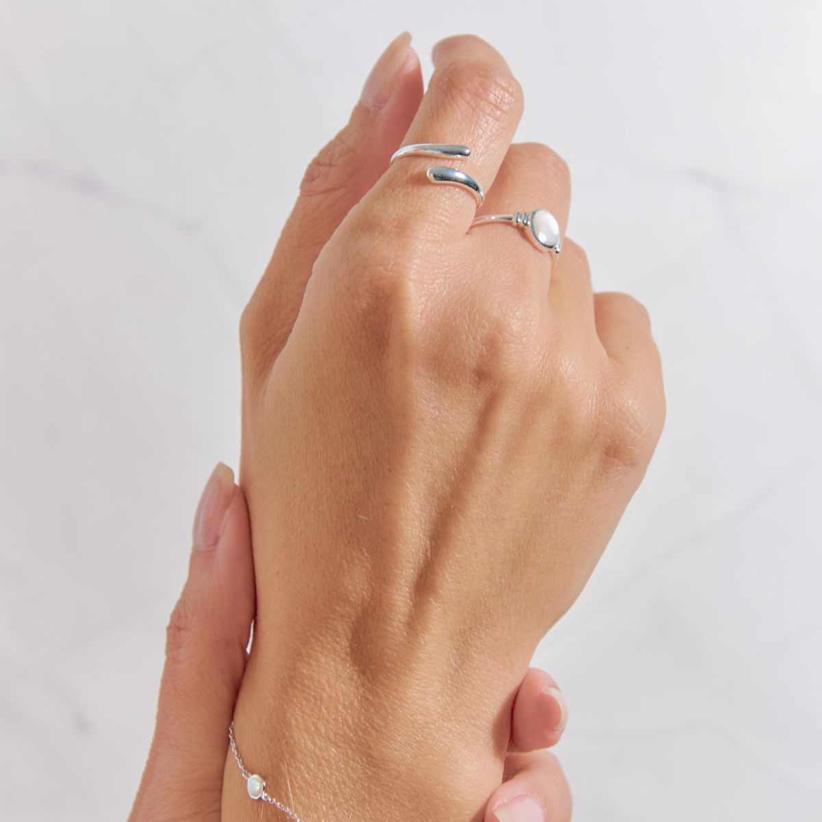 Hand wearing two silver rings on a light gray background