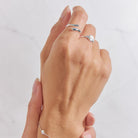 Hand wearing two silver rings on a light gray background