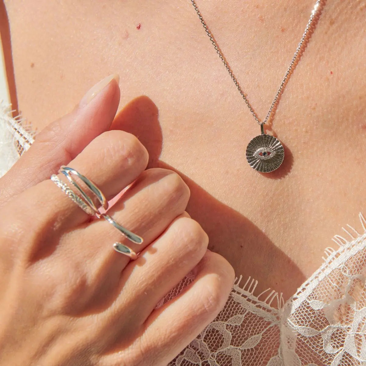 Silver ring and necklace on a person's hand with lace fabric in the background