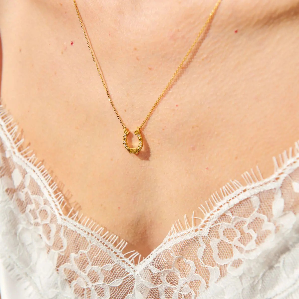 Gold necklace with a pendant worn by a person in a white lace garment.