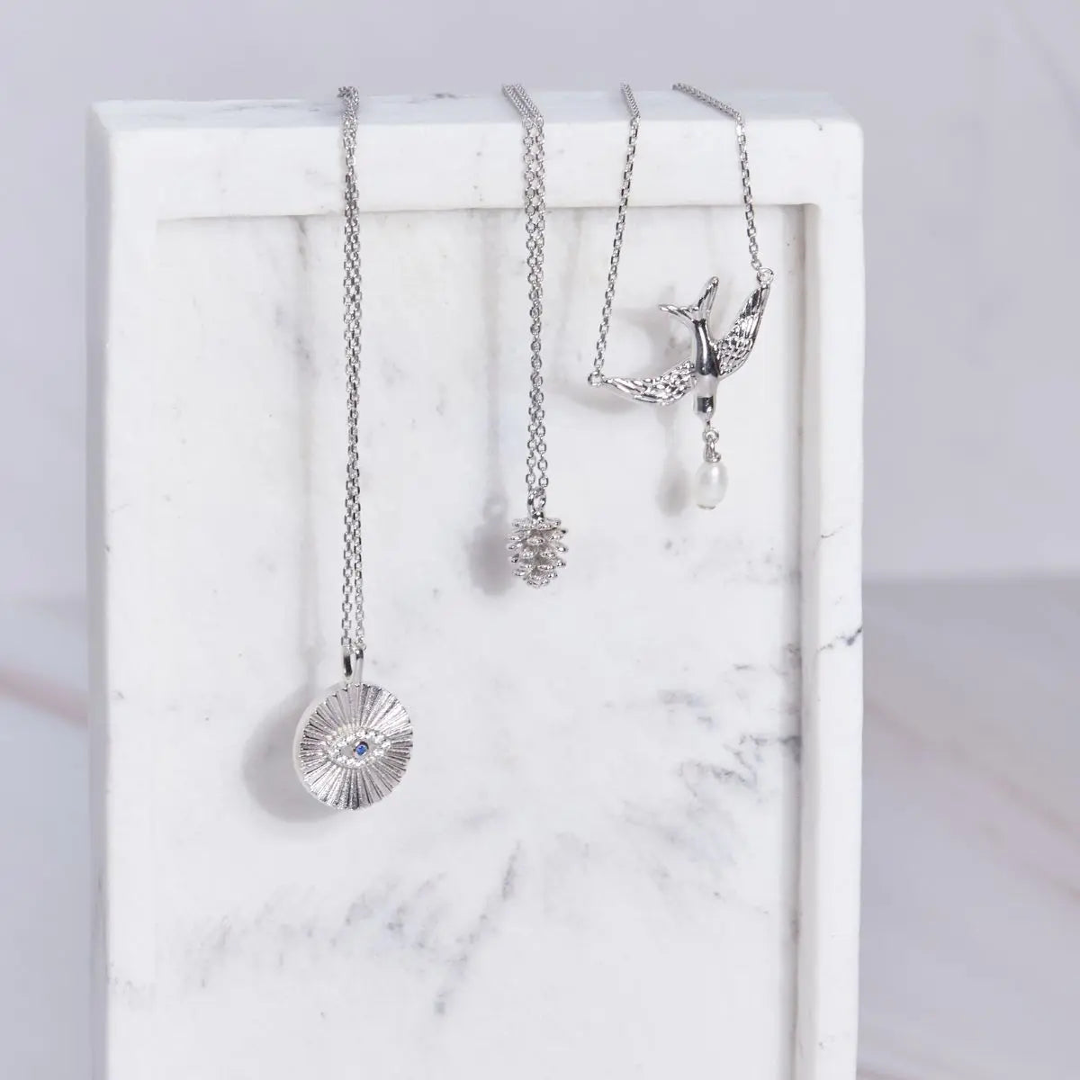 Three silver necklaces on a marble surface