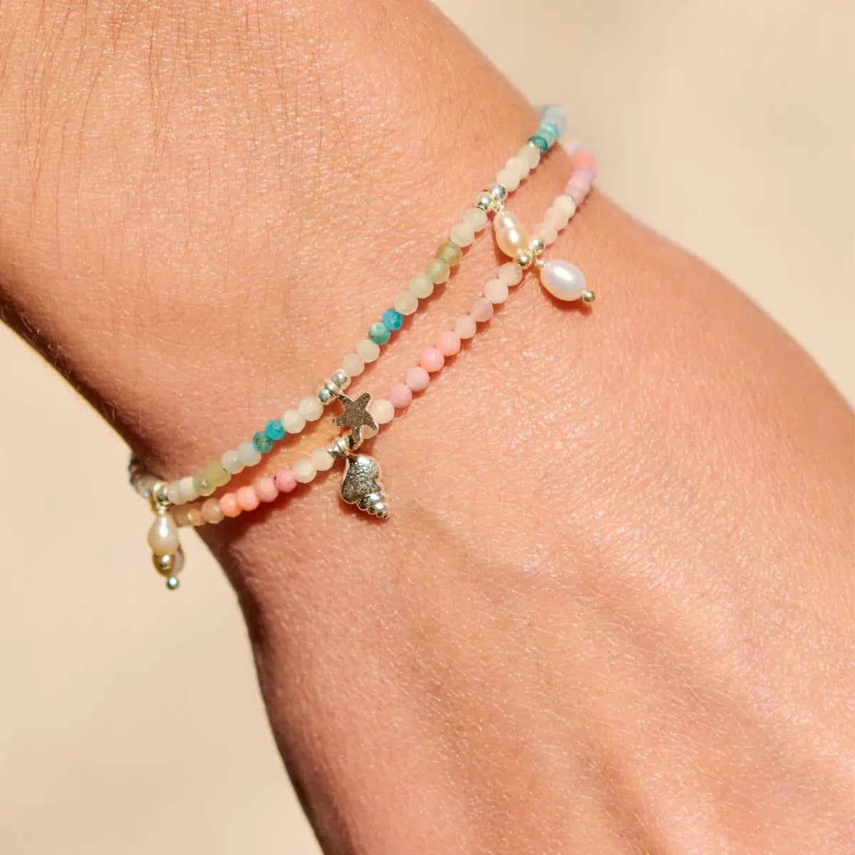Multistrand beaded bracelet with charms on a wrist against a beige background