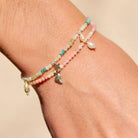 Multistrand beaded bracelet with charms on a wrist against a beige background