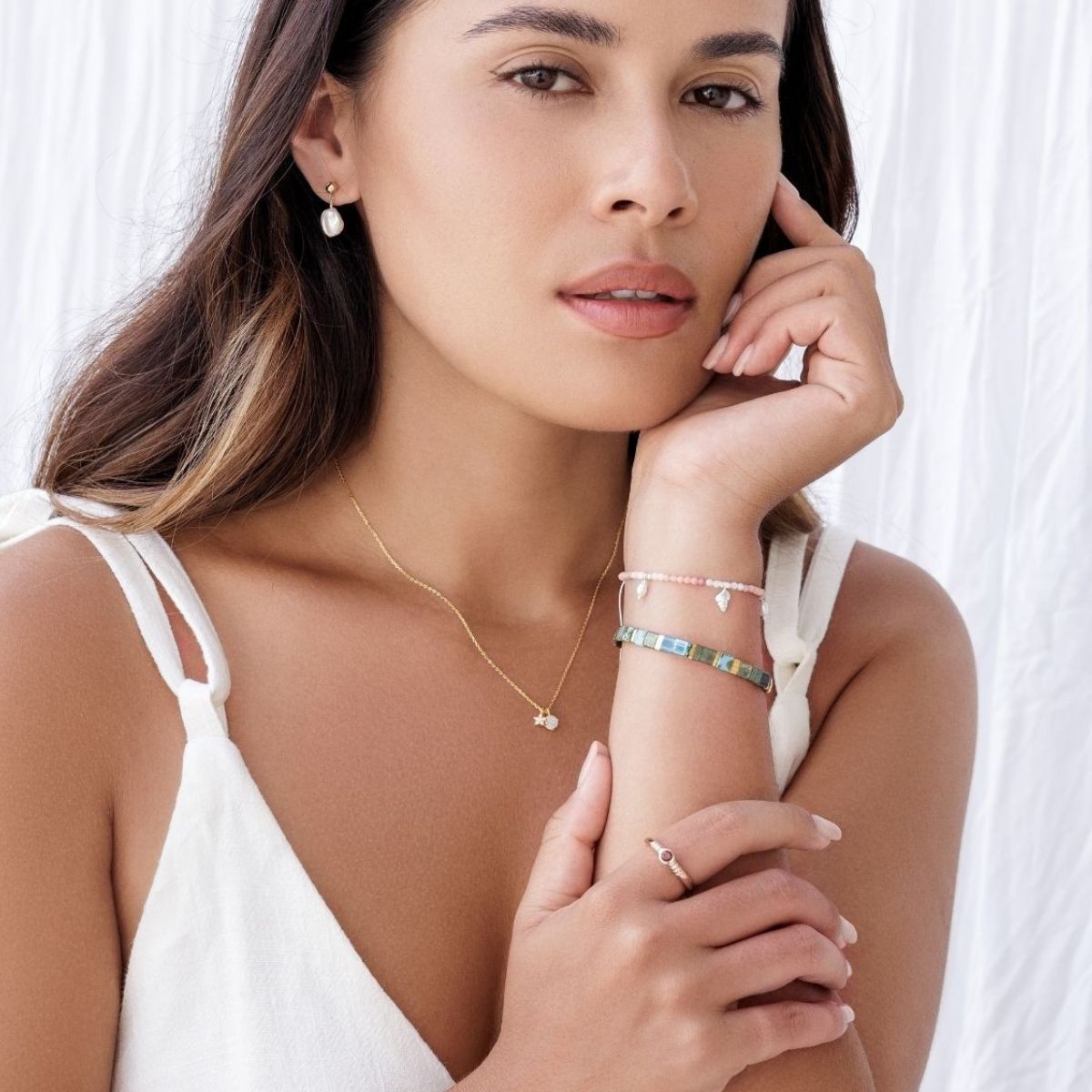 Woman wearing gold necklace, ring, and bracelets on a white background