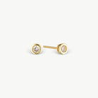A pair of gold stud earrings with round bezel settings holding clear round-cut gemstones, shown on a clean off-white background.