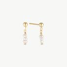 A pair of gold post earrings with a small gold ball at the top and three dangling white pearl beads, shown on a clean off-white background.