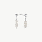 A pair of silver drop earrings featuring three stacked white pearl beads on each earring, shown against a plain off-white background.
