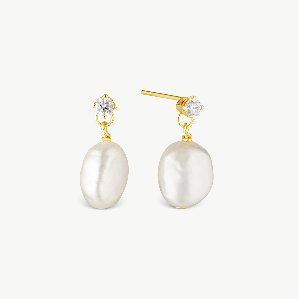 A pair of gold drop earrings featuring large, irregular white baroque pearls and a small clear round-cut gemstone at the top, set against a plain off-white background.