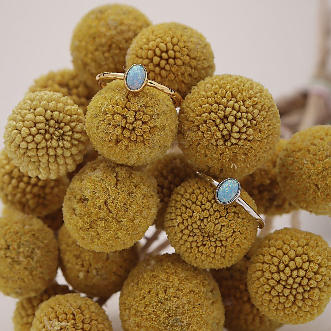 Two rings with oval blue-green stones in gold and silver settings, displayed on a cluster of dried yellow-brown pom-pom flowers.