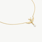 A delicate gold chain necklace featuring a small bird charm with a dangling white pearl, shown against a clean off-white background.