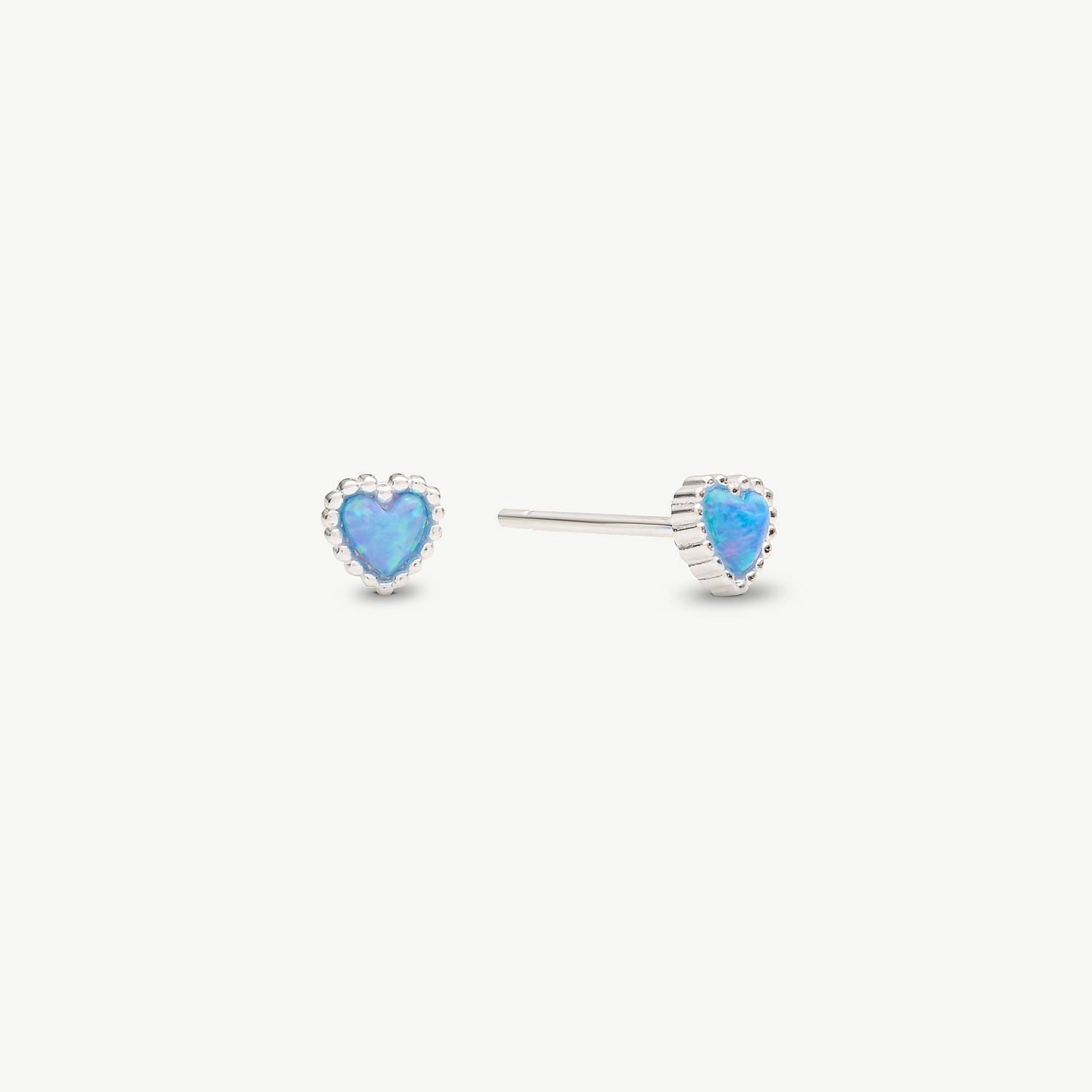 A pair of silver heart stud earrings with vibrant blue opal centers, shown on a clean off-white background.