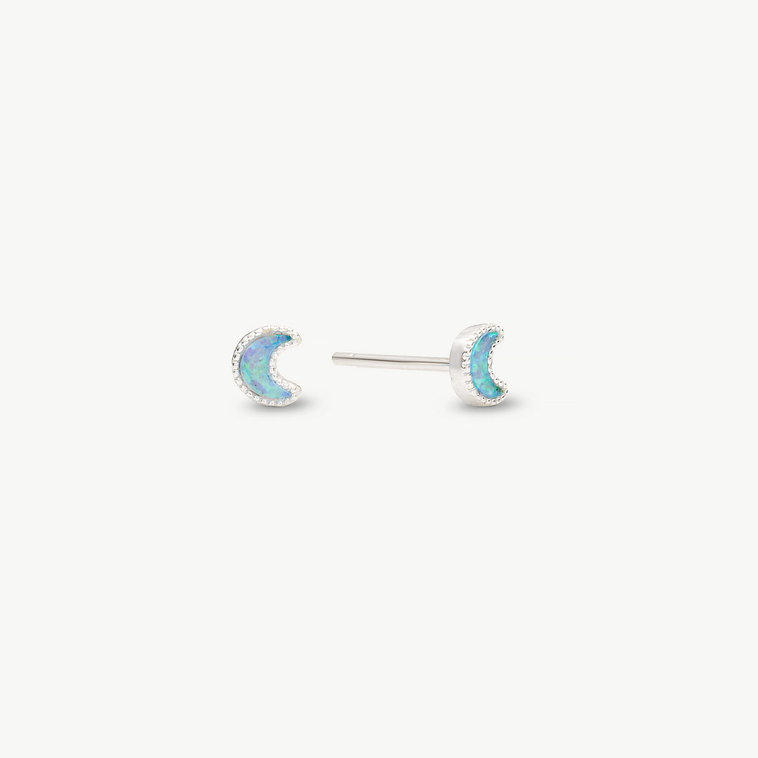A pair of silver crescent moon stud earrings with iridescent blue-green opal inlays, shown on a clean off-white background.