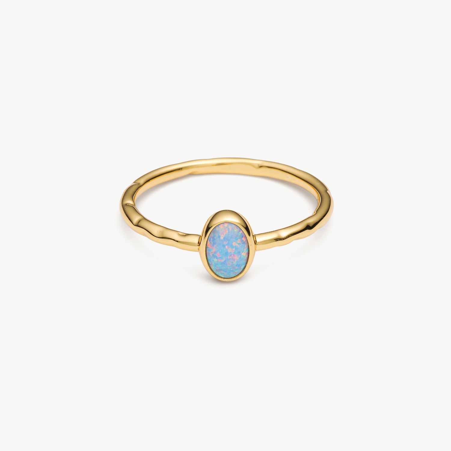 A gold ring with a textured band and an oval-shaped light blue opal center stone, shown on a clean off-white background.