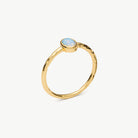 A gold ring with a small oval light blue opal gemstone, shown on a clean off-white background.